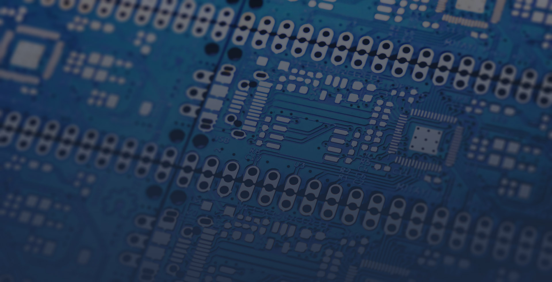 Close up image of the underside of a neatly arranged grid of blue circuitboards, the dark blue of the circuit traces and the light grey of the component contacts standing out against the rest of the board.